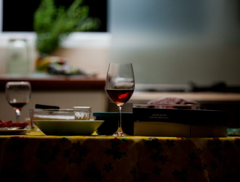 A single glass of red wine sits on a kitchen table in muted evening light.